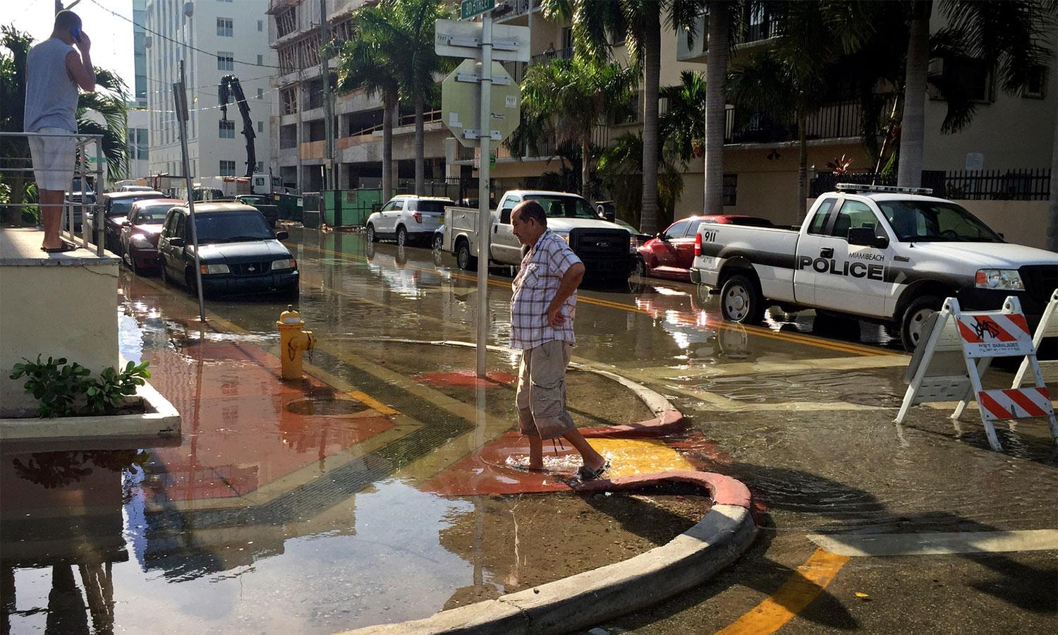 Man walks through water on flooded Miami street.