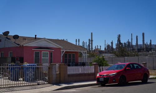 Una casa color rosa y auto rojo al lado de una refinería